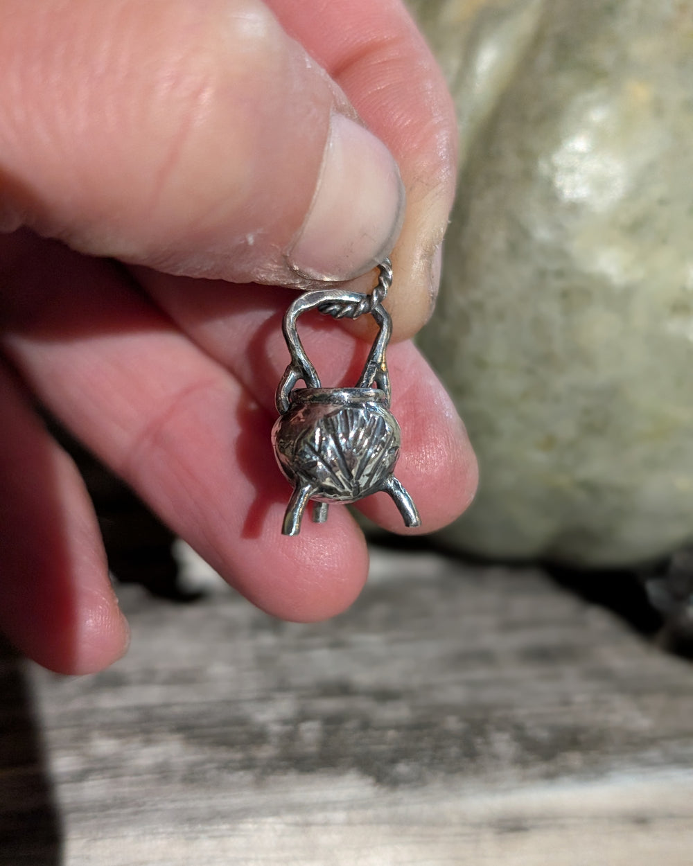 Ciondolo mini calderone Livia Fior di Ipomea in argento 925 tenuto tra le dita, con una zucca sullo sfondo