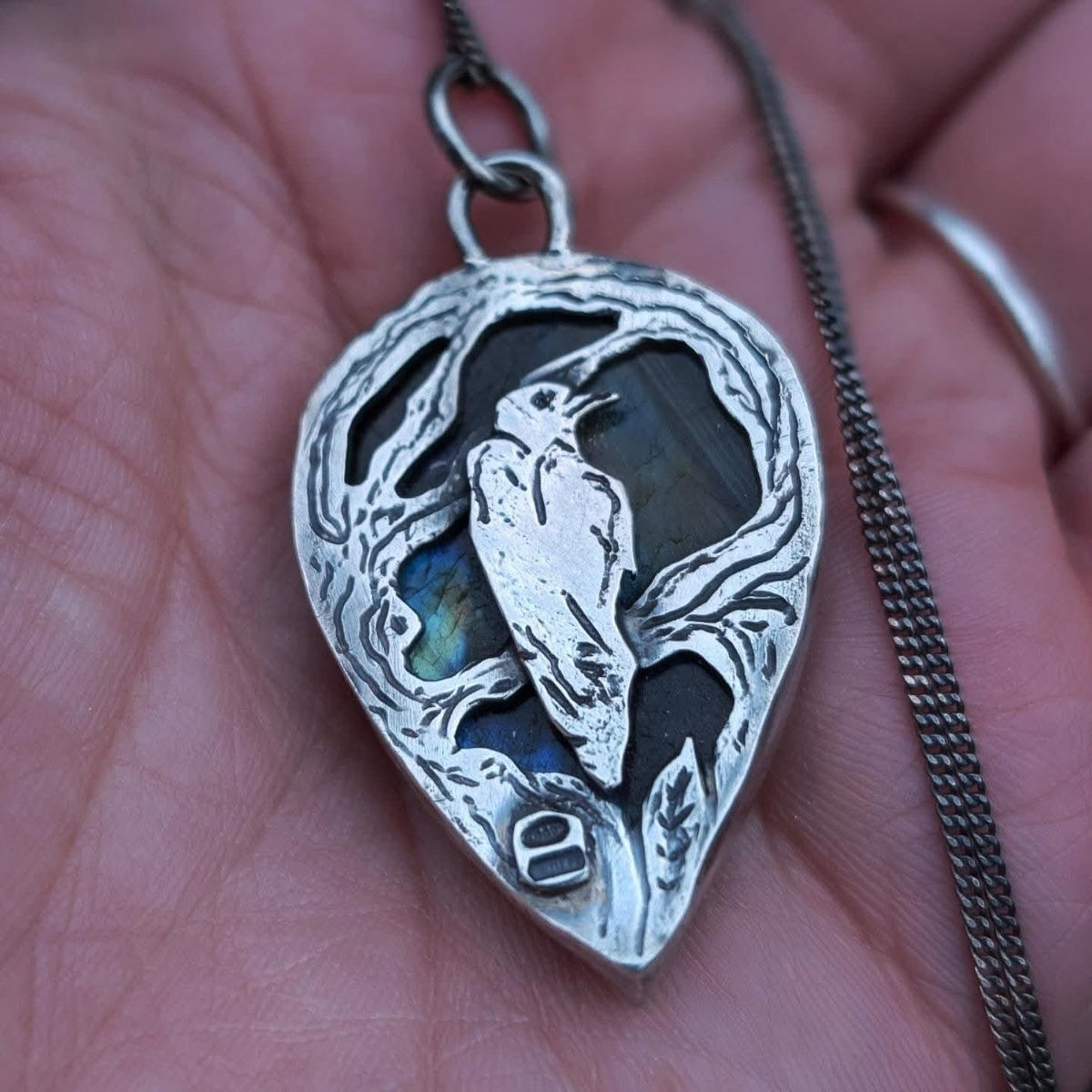 Dettaglio del ciondolo Il Bosco del Corvo: corvo inciso in argento 925 davanti alla labradorite