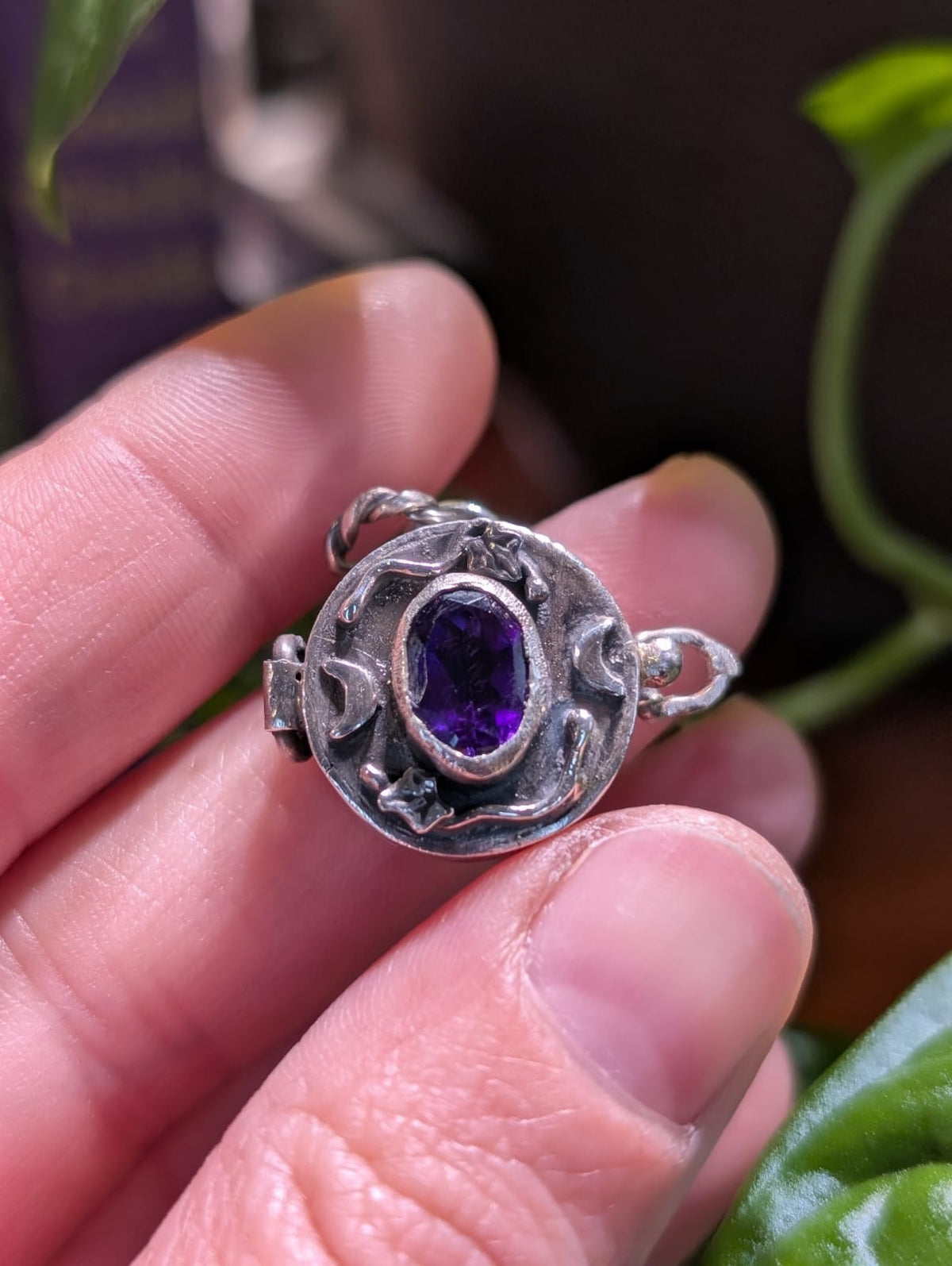 The Witch's Secret held between the fingers: the oval amethyst set between ivy and two crescent moons