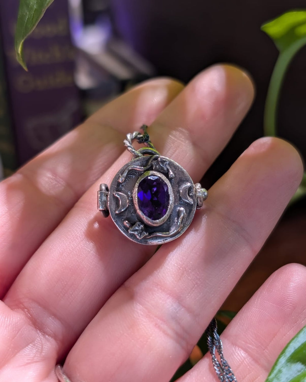 Medaglione Il Segreto della Strega chiuso, in argento 925 brunito con ametista viola sfaccettata, rametti di edera e lune crescenti, appoggiato sulla mano
